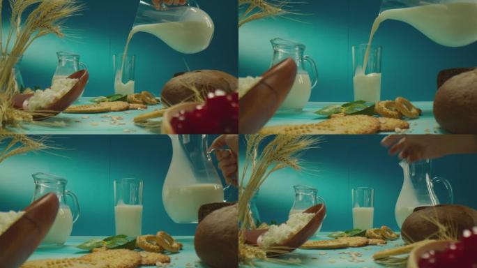 装饰桌子的美丽组成，带有牛奶，乳制品，烘焙产品，浆果，蓝色背景上的花朵。男人从水罐里把牛奶倒进玻璃杯