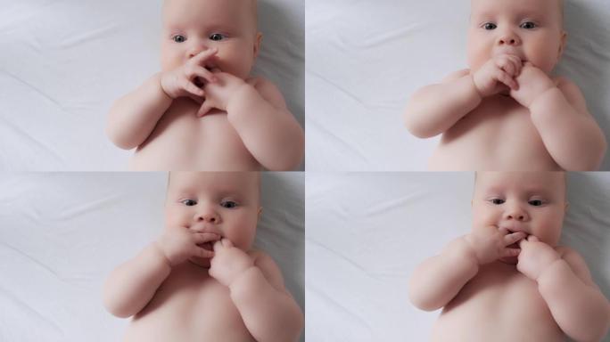 自信可爱的裸婴躺在舒适的白色床单上嚼手指