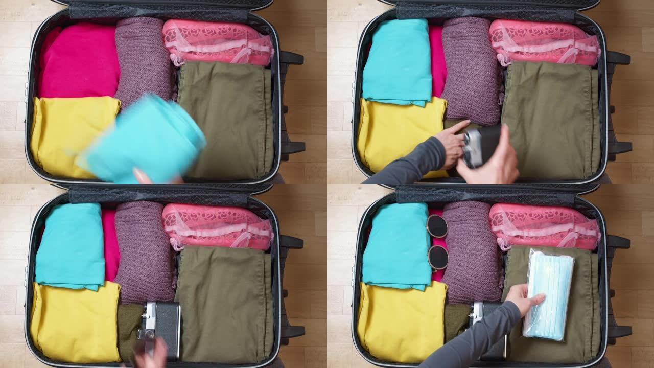 女人的手在手提箱里装着旅行用的东西，还有防护口罩。顶视图。