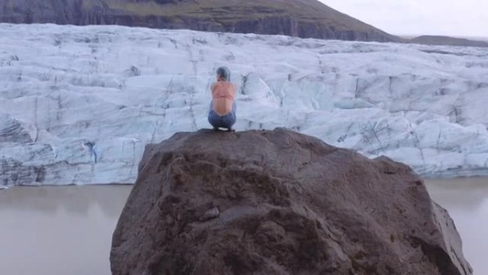 女人的无人机蹲在冰川上的岩石上