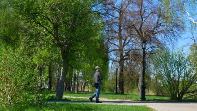 一个戴着蓝色帽子的胡须的男人正在绿树丛中的公园里散步