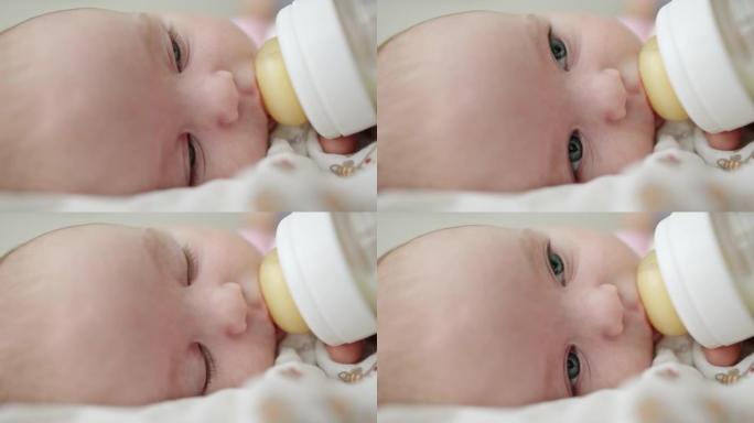 满足的小婴儿从瓶子里喝配方奶粉，眨着眼睛，放心地看着喂食的人