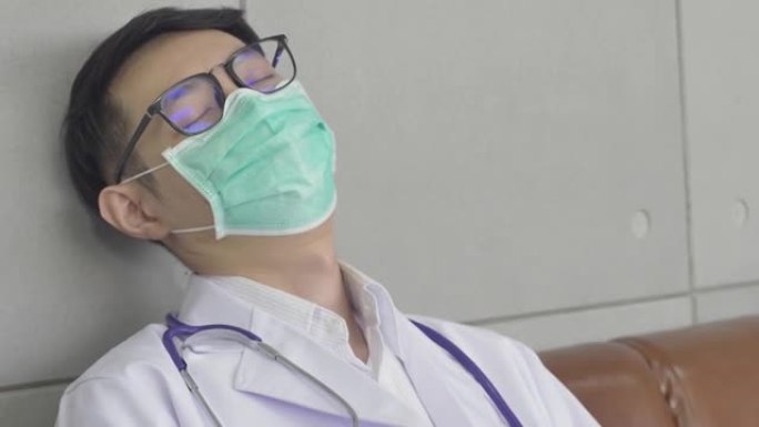 手持照片中，一位年轻医生戴着医用口罩和眼镜的工作精疲力尽，坐在沙发上。