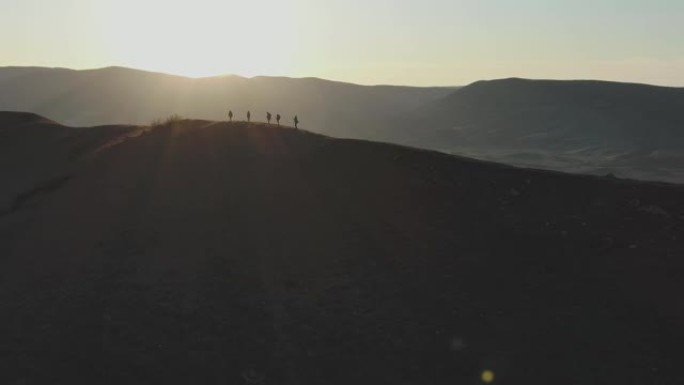 鸟瞰图。一群志同道合的人在地平线和日落的背景下，沿着平坦的山顶行走。