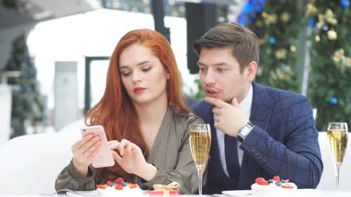 一对恋爱中的情侣在餐厅浪漫约会。浏览红头发女孩智能手机上的在线菜单