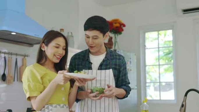 恋爱中的年轻夫妇在家里浪漫的气氛中帮忙做饭，带着微笑的脸看着相机。