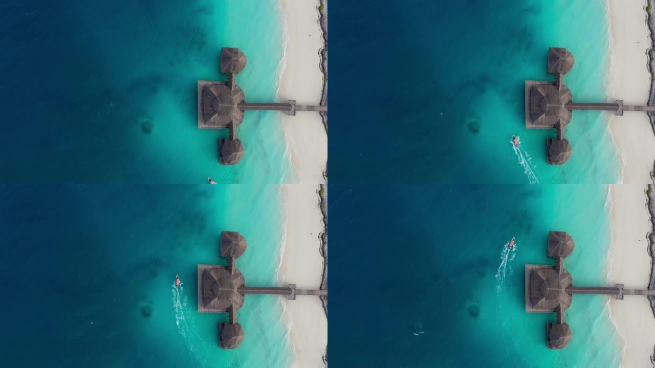在坦桑尼亚桑给巴尔岛上，白色沙洲海滩附近的深蓝色海浪对移动的摩托艇进行了4k空中拍摄，高跷小屋被碧绿