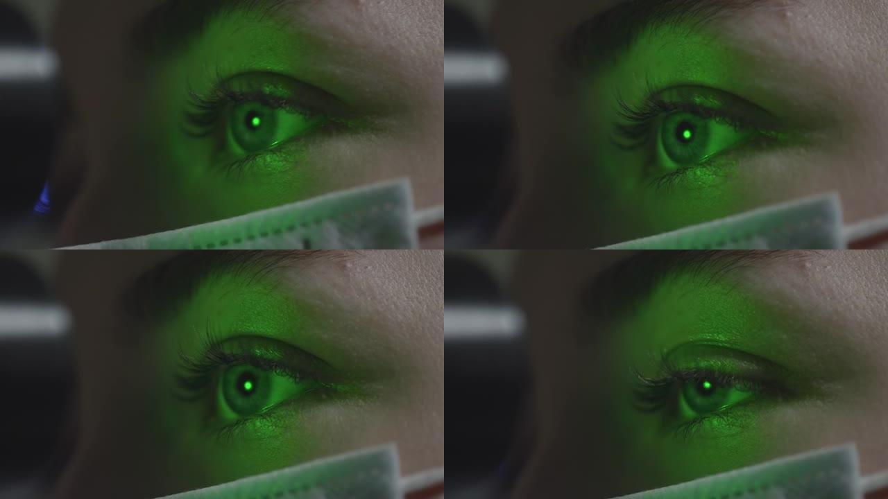 MACRO:一位戴着医用口罩的妇女在与眼科医生预约时检查眼睛。一束绿色的激光射进瞳孔。眼科治疗-一位