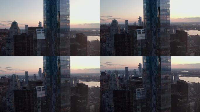 空中无人驾驶飞机在曼哈顿天际线的巨大摩天大楼大楼旁升起，日落时灯光闪烁，空中建立