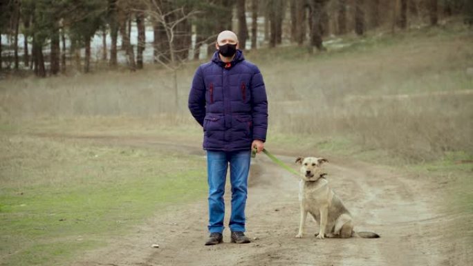 男性黑色防护抗电晕病毒面罩不动站在户外，狗在森林附近冬季在检疫上自我隔离