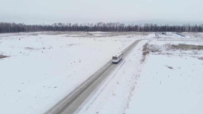 无人机飞到公共汽车后面。冬季道路以白雪覆盖的田野为背景，鸟瞰。西伯利亚针叶林冬季的油田