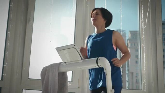 在跑步机上跑步。在家健身。年轻女子的肖像正在家里跑步智能教练，做有氧运动。女运动员在家中保持健康