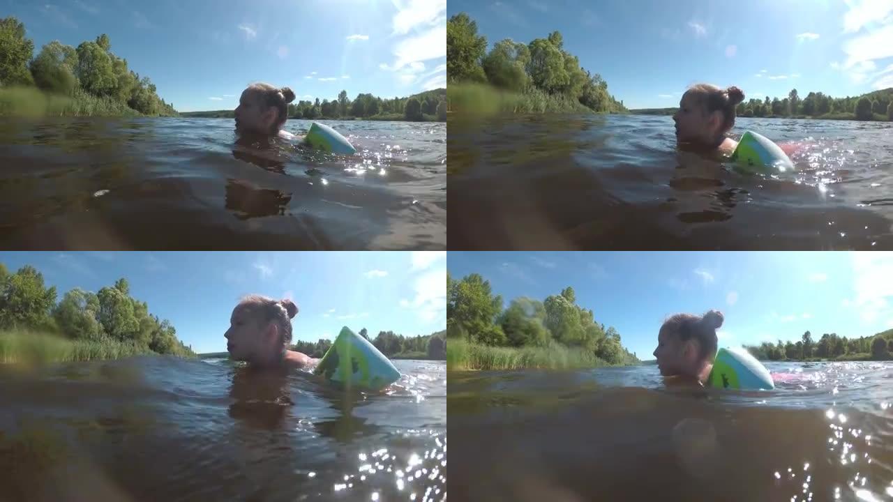 一个孩子，一个小女孩，在阳光明媚的夏日里，学会在河里游泳，并在充气臂章中游泳。健康生活方式的概念。暑