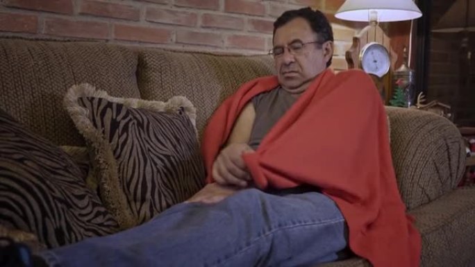 西班牙裔高级男子躺在沙发上，毯子因可能的新型冠状病毒肺炎疾病而感到不适