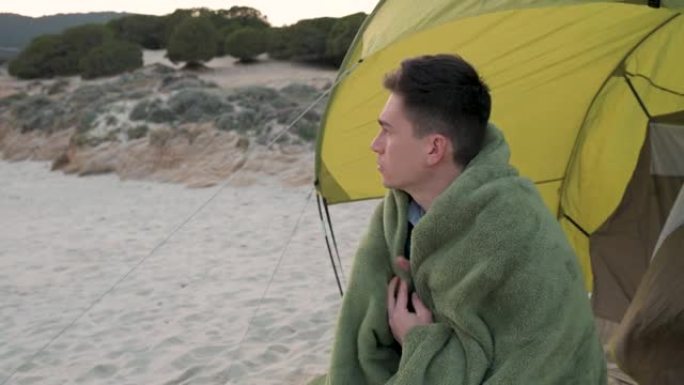 年轻的拉丁男子晚上在多风的海滩上披着毯子，用自信的脸移开了目光。