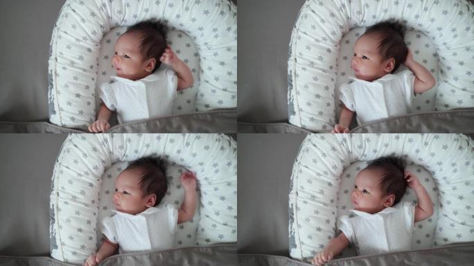 纯真亚洲婴儿婴儿在床上移动手的俯视图和灰色背景。