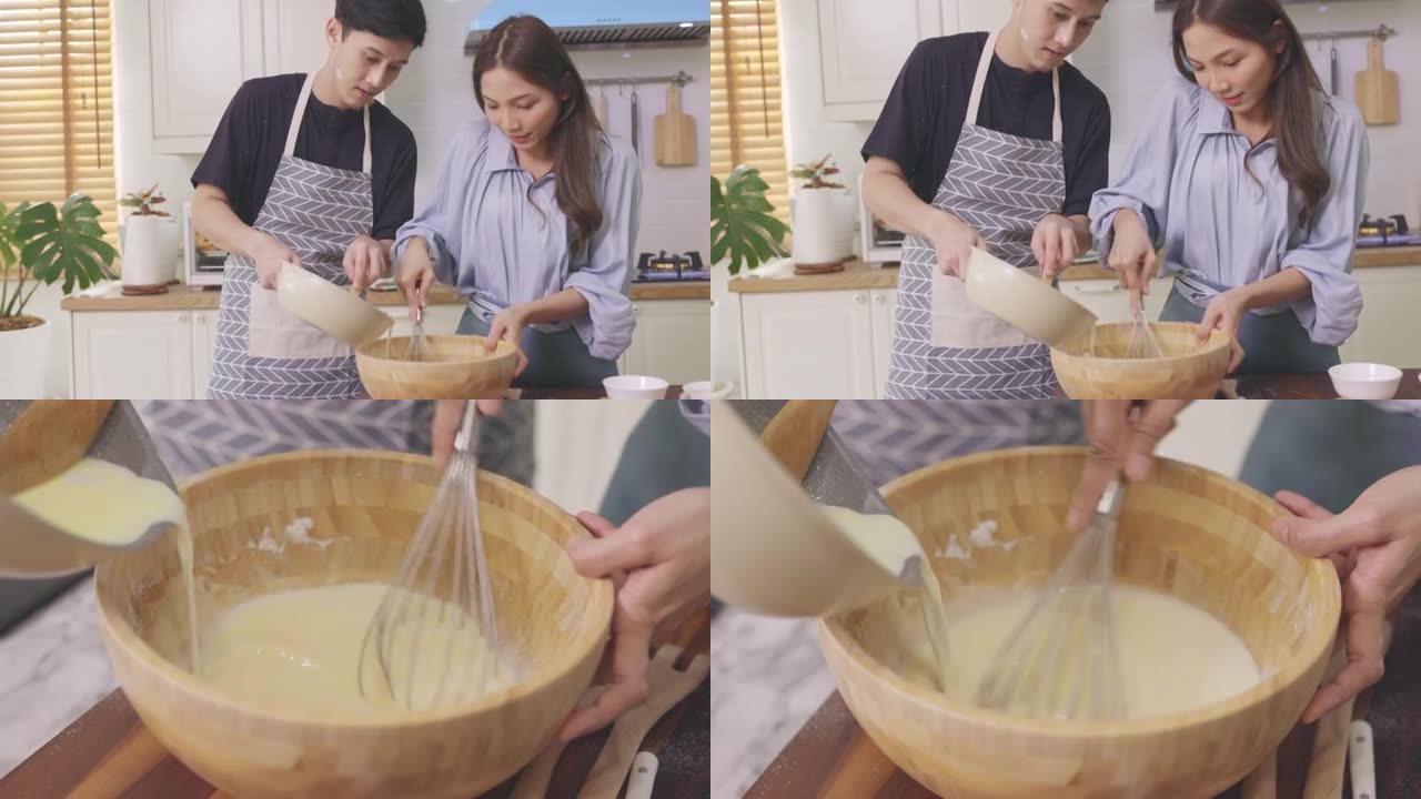 亚洲夫妇在家里的厨房里互相帮助，在浪漫的气氛中制作面包店。年轻人一起工作，将配料混合在木碗中，然后将