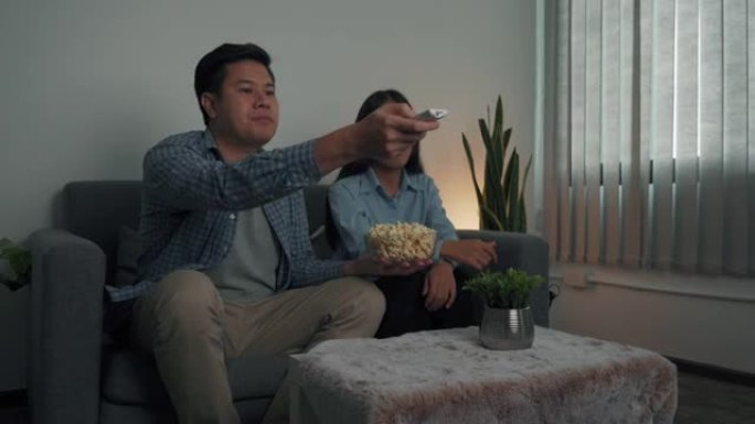 亚洲夫妇晚上在客厅边吃爆米花边看连续剧。