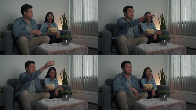 亚洲夫妇晚上在客厅边吃爆米花边看连续剧。