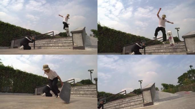 一名亚洲男子在滑板公园白天拍摄他的朋友在楼梯上滑板的照片的慢动作镜头