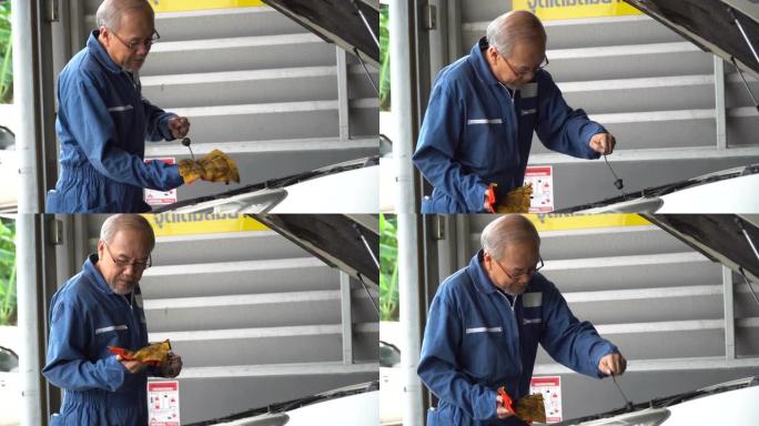 亚洲机械师高级男子在汽车维修服务中心的车间检查油位并擦拭汽车的油尺。汽车工程师老人正在检查车辆详细信