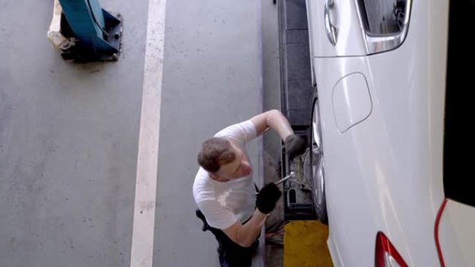 工人男子汽车服务人员的俯视图在工厂服装修理汽车车轮和轮胎车库停车场的工作人员。在备件运输工业仓库工作