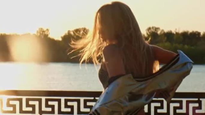 女孩摇着头发站在夕阳下的路堤上