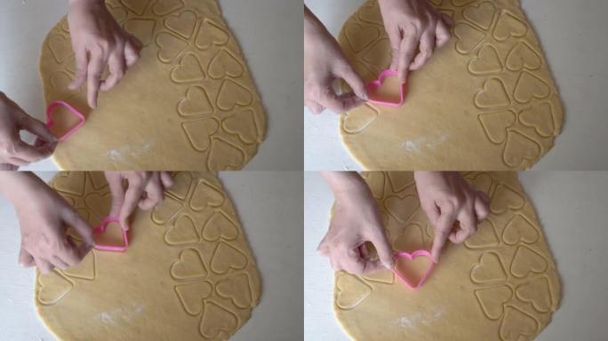 特写镜头，女性的手从生面团坯料中切出心形饼干。一个女人在家庭厨房做饭。小型家庭企业的概念。不露面。顶