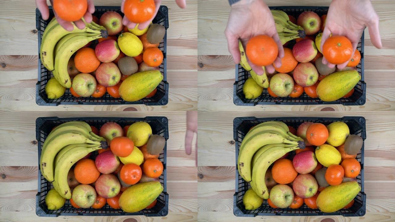 一个人以慢动作将橘子扔在一盒热带异国水果上。在木制背景上，俯视图。