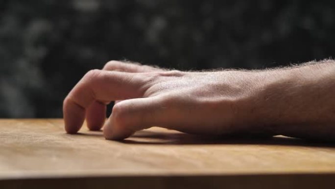 一只男性的手用指甲刮伤了一块木板。
