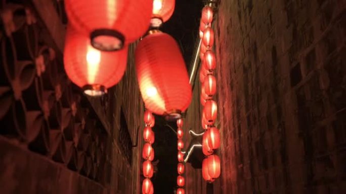 沿着右边的石墙向前走，穿过中国古庙的狭窄走廊。点燃了红灯笼，四处悬挂着照明灯。传统装饰，节日庆典