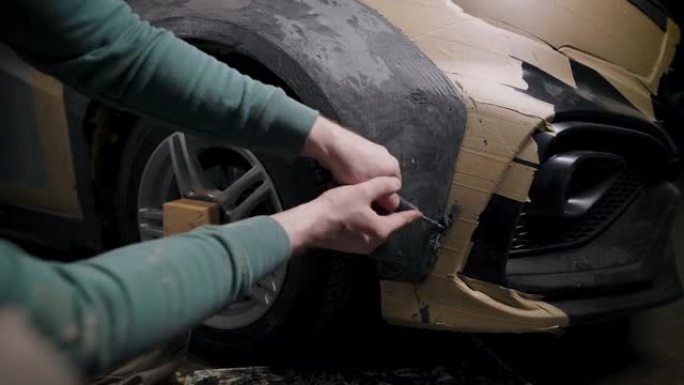 工人正在车库的车身上塑造粘土细节，为汽车进行投影调整，用塑料刀工作