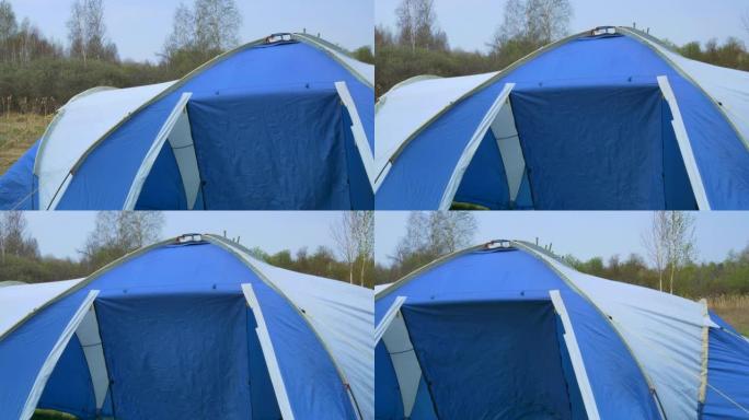 一个大的蓝色和白色的帐篷在大自然中布置，在风中摇曳，在一片春天的森林后面