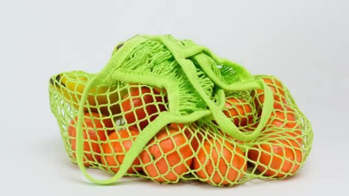 女性手将一个可重复使用的纺织细绳袋，上面装有成熟的橘子和橘子，放在白色表面上，拒绝使用塑料