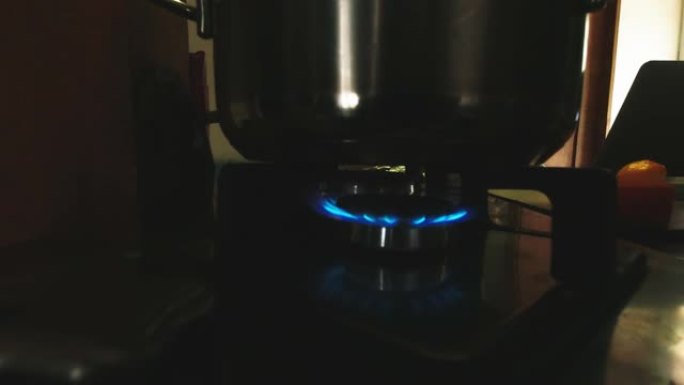 在家里昏暗的灯光下，用银锅燃烧的气体烹饪火焰的特写侧视图。准备食物和时间概念copyaste背景