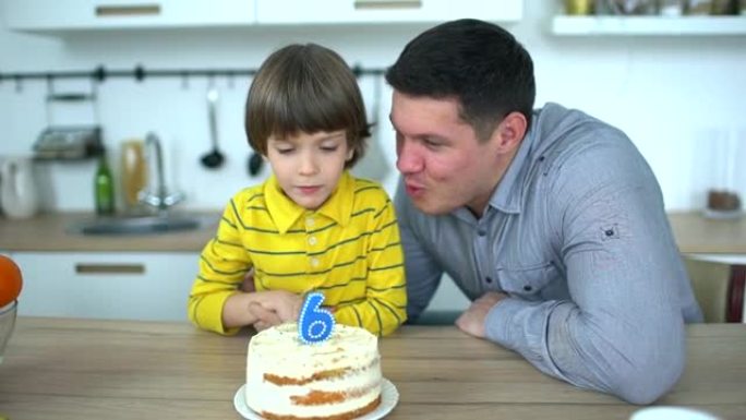 非常可爱的男孩用蛋糕和快乐的父亲庆祝他的生日。6年生日快乐。小男孩在家吹灭生日蛋糕上的蜡烛