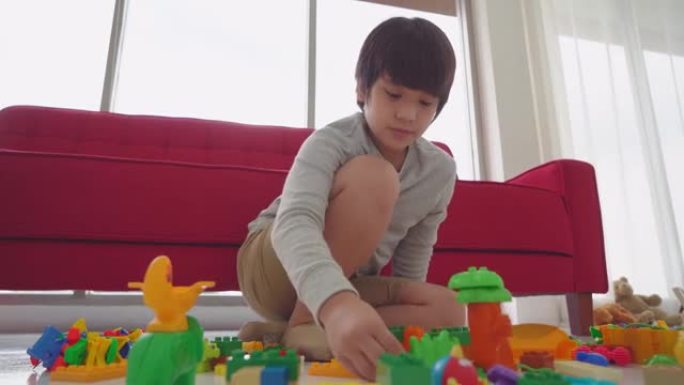 亚洲小男孩正在地板上建造彩色砖块玩具，背景是客厅沙发。
