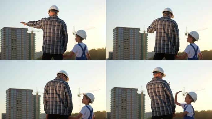 小男孩和他的父亲工程师建筑设计师，戴着安全帽，在现场背景新建筑和建筑起重机上