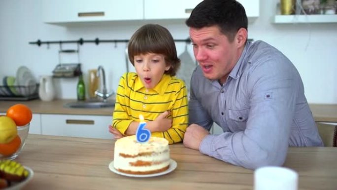 非常可爱的男孩用蛋糕和快乐的父亲庆祝他的生日。6年生日快乐。小男孩在家吹灭生日蛋糕上的蜡烛。父子俩一