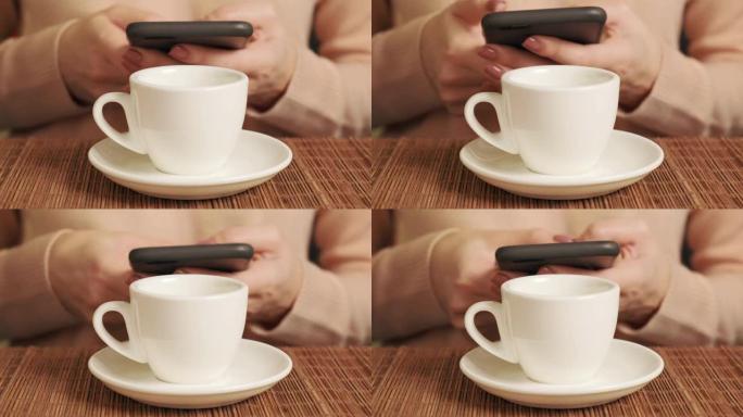 一个女人手里拿着手机，在一个白色的杯子里喝咖啡。