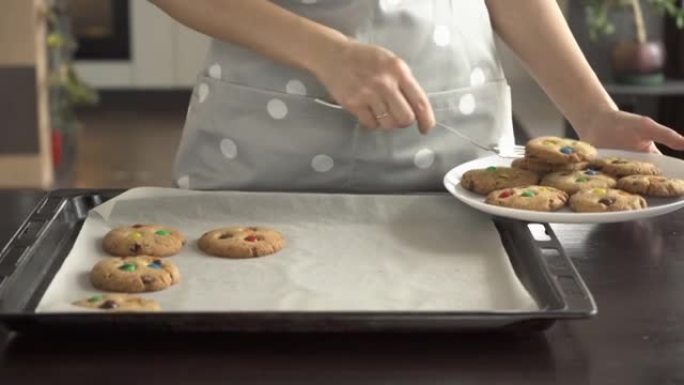 一名妇女从烤盘中取出带有彩色M & Ms糖果的饼干