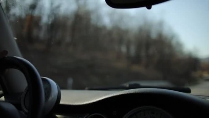 一个男人开车的手的特写。驾驶时从车内通过挡风玻璃观看。太阳的光线穿过挡风玻璃，照亮方向盘和仪表板。