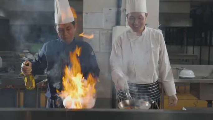 两名厨师在厨房用燃烧的火烹饪食物