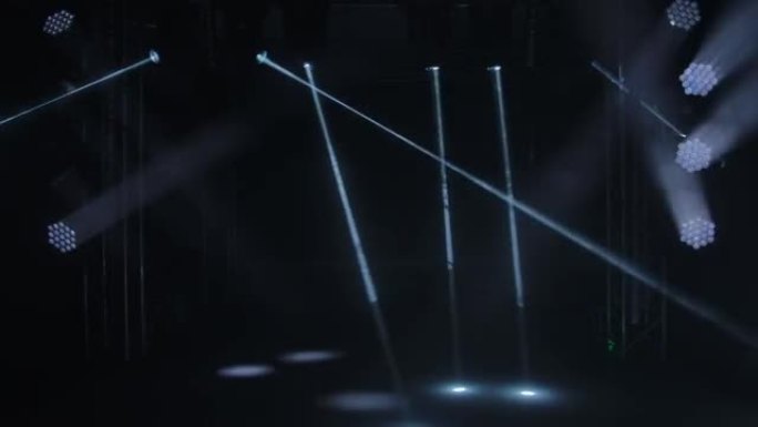 黑色演播室背景上舞台灯光的动态白色光束。探照灯旋转，转动并发出光束。全息图显示。假日和聚会的照明设备
