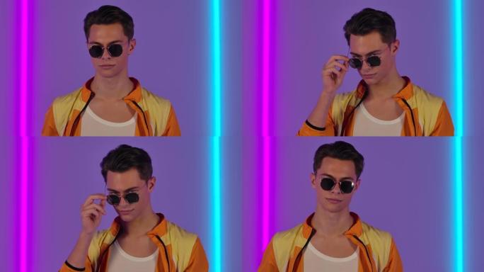 时尚男人戴着太阳镜嬉戏地看着相机的肖像。穿着黄色夹克的男性时装模特在明亮的霓虹灯的背景下，在黑暗的工