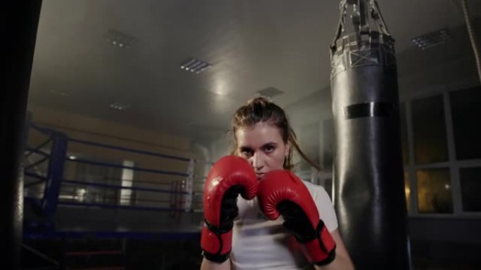 年轻的职业拳击女孩穿着拳击手套积极地滑入相机镜头晚上穿着运动服在健身房训练