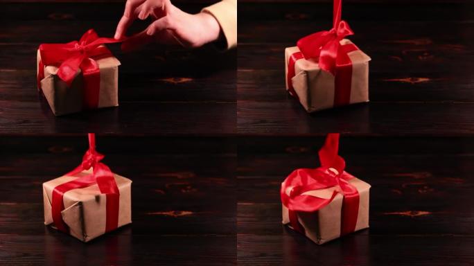 女人的手解开礼品盒上的红丝带。超级慢动作