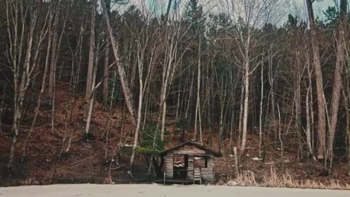 被遗弃的摇摇欲坠的小屋在冬季森林里结冰的湖畔。缩小