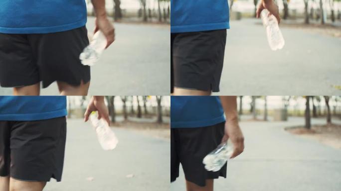 年轻的亚洲男子运动员在公园跑步锻炼后走路和拿着水瓶。