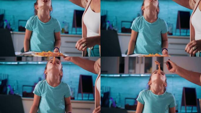 一个年轻女孩以有趣的方式吃意大利面，幸福和玩弄食物的镜头。母亲的手喂女孩意大利面